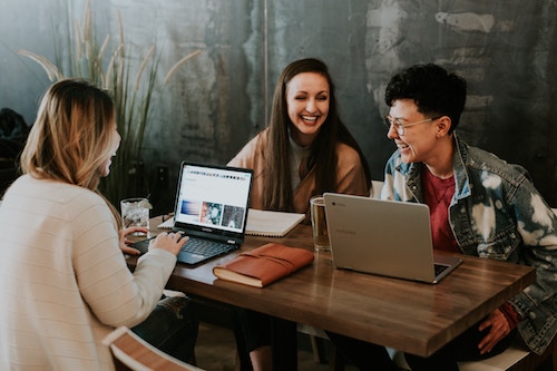 Photo: group of people seated at a table in front of laptops and laughing