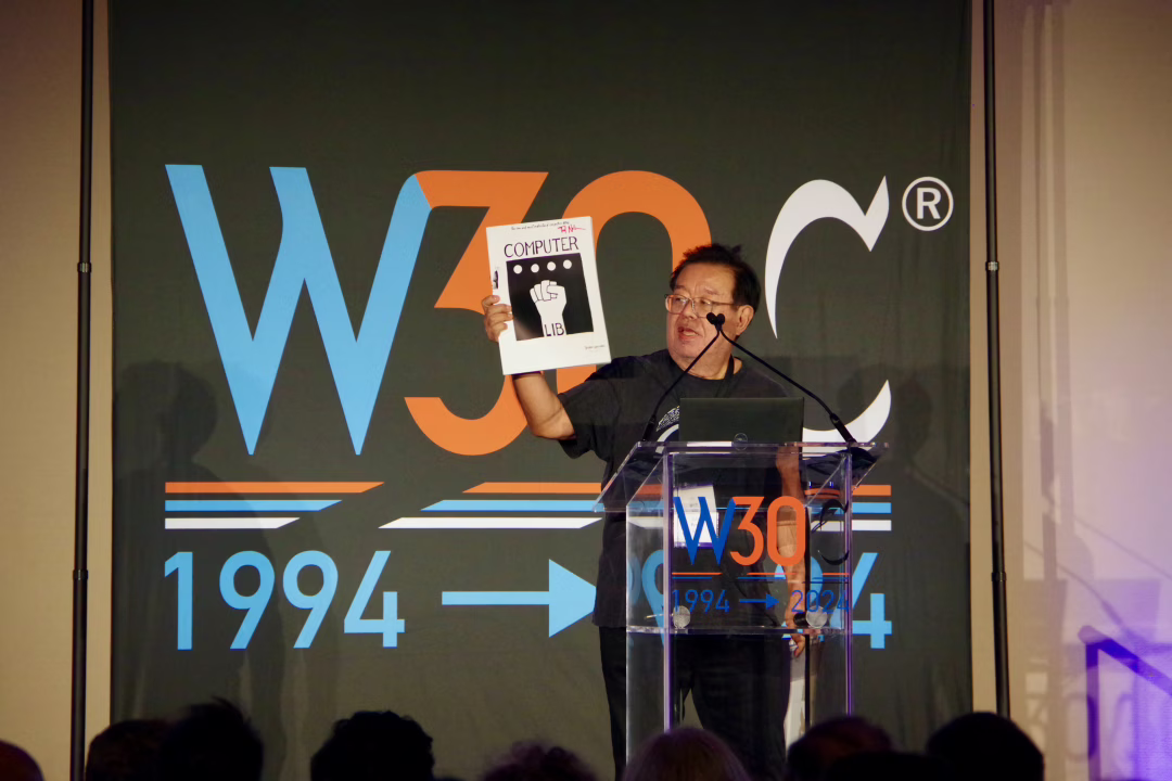 Speaker on the podium holds up a book titled ‘Computer lib’.