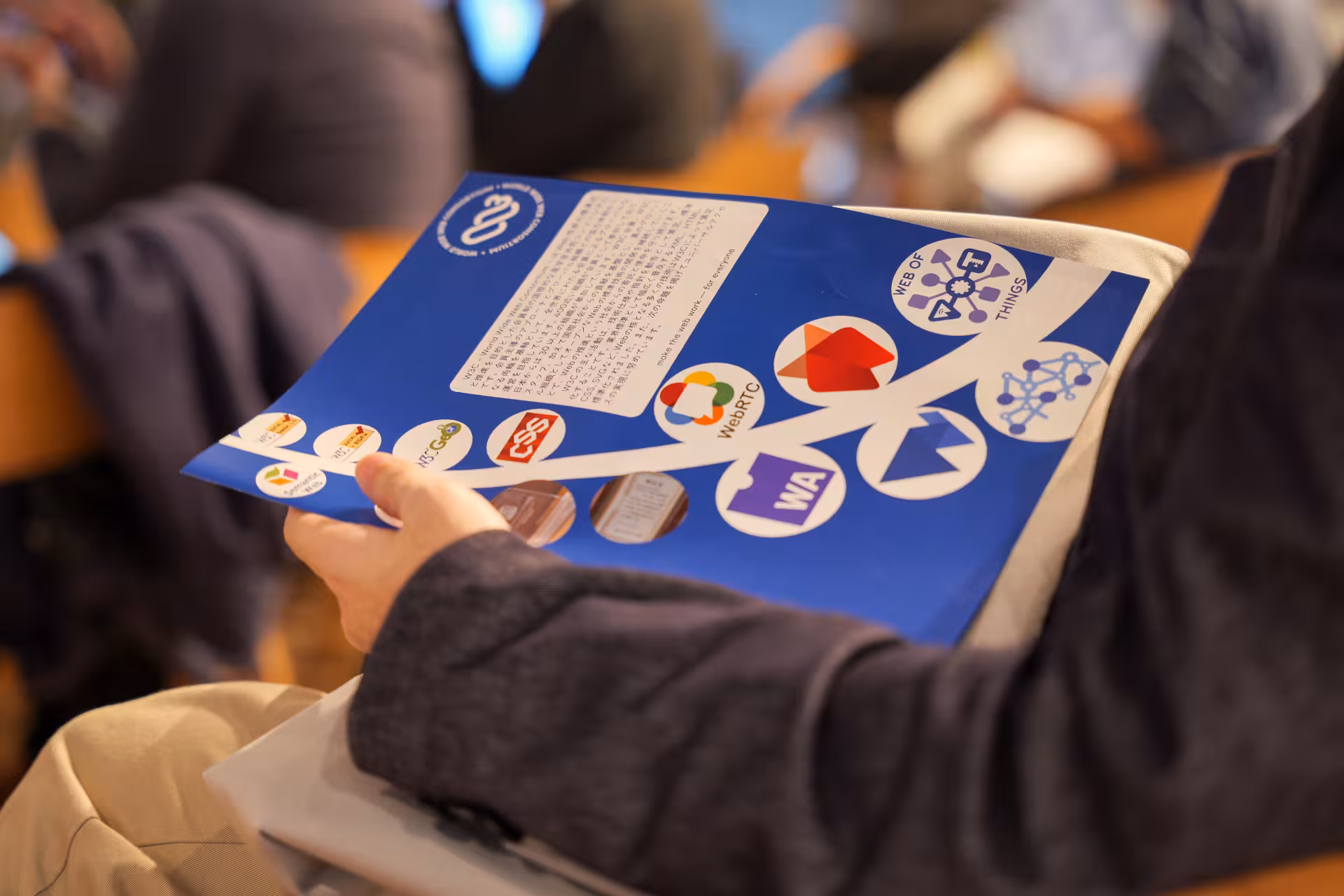 Close-up of a printed leaflet showing several W3C technologies logos being held on someone's lap