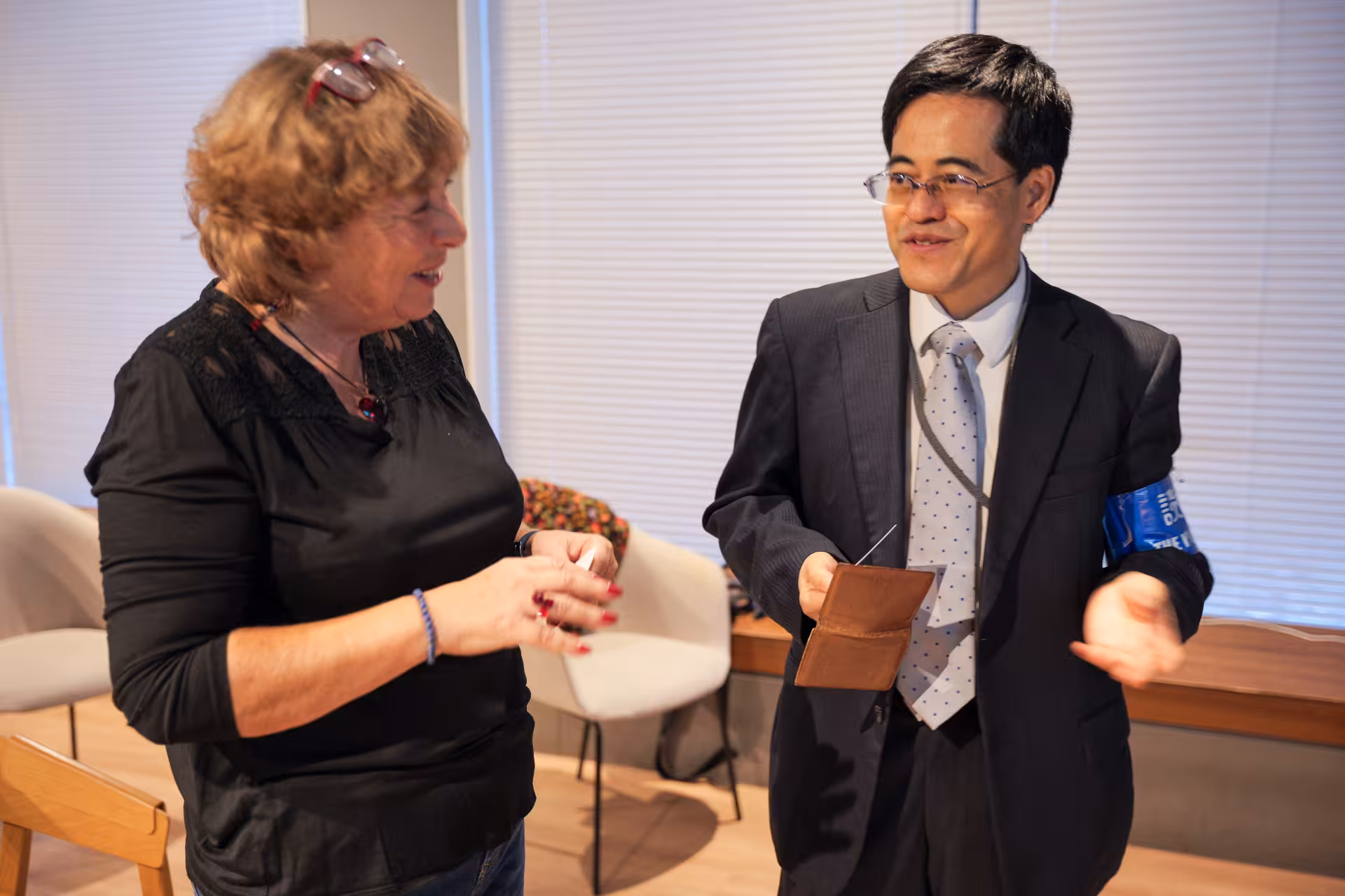 A woman and a man in conversation. They appear to be exchanging business cards. The man in the business suit is wearing a blue armband.