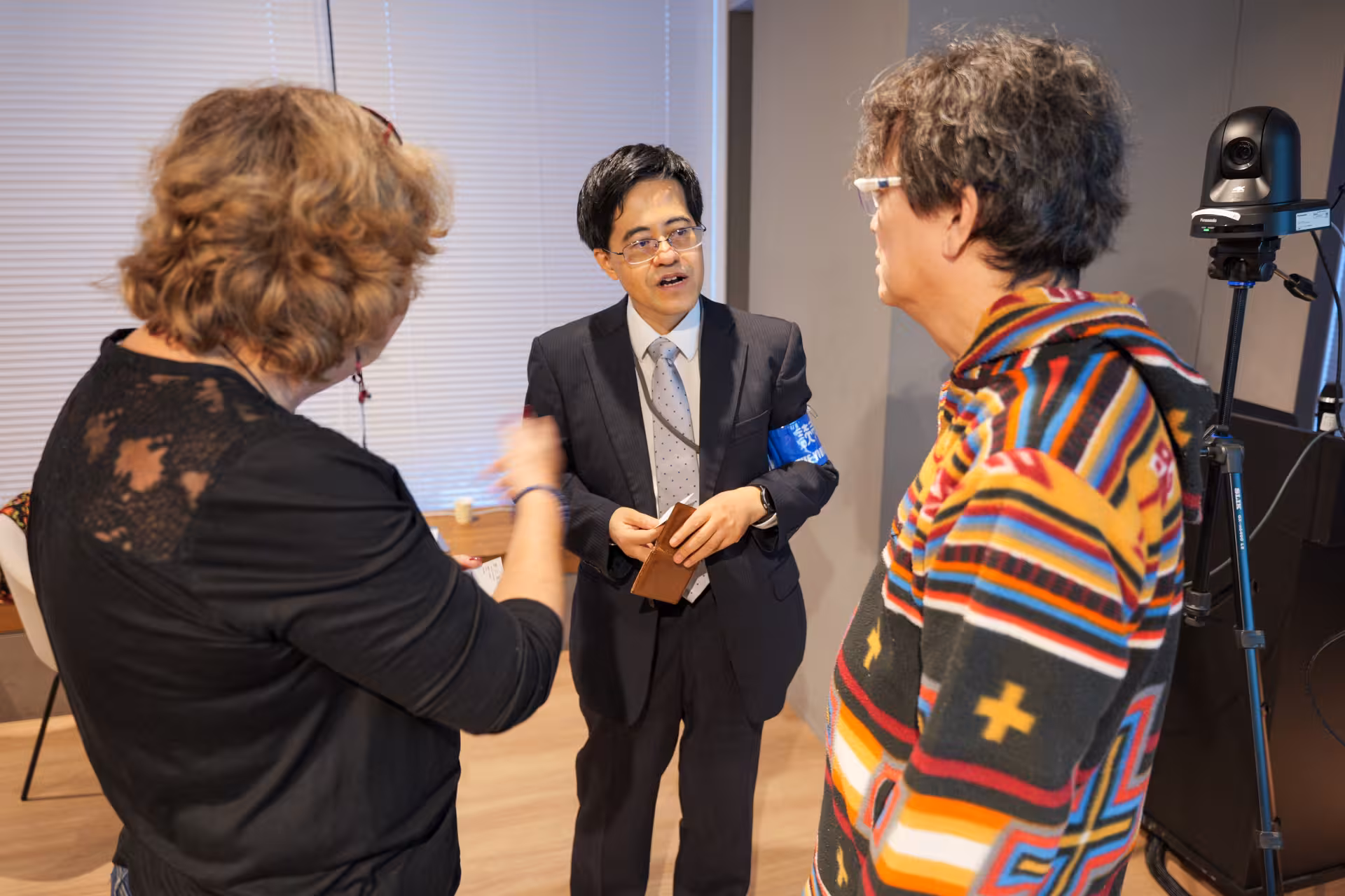 Three persons in a conversation in a room where a camera is setup in a cornier